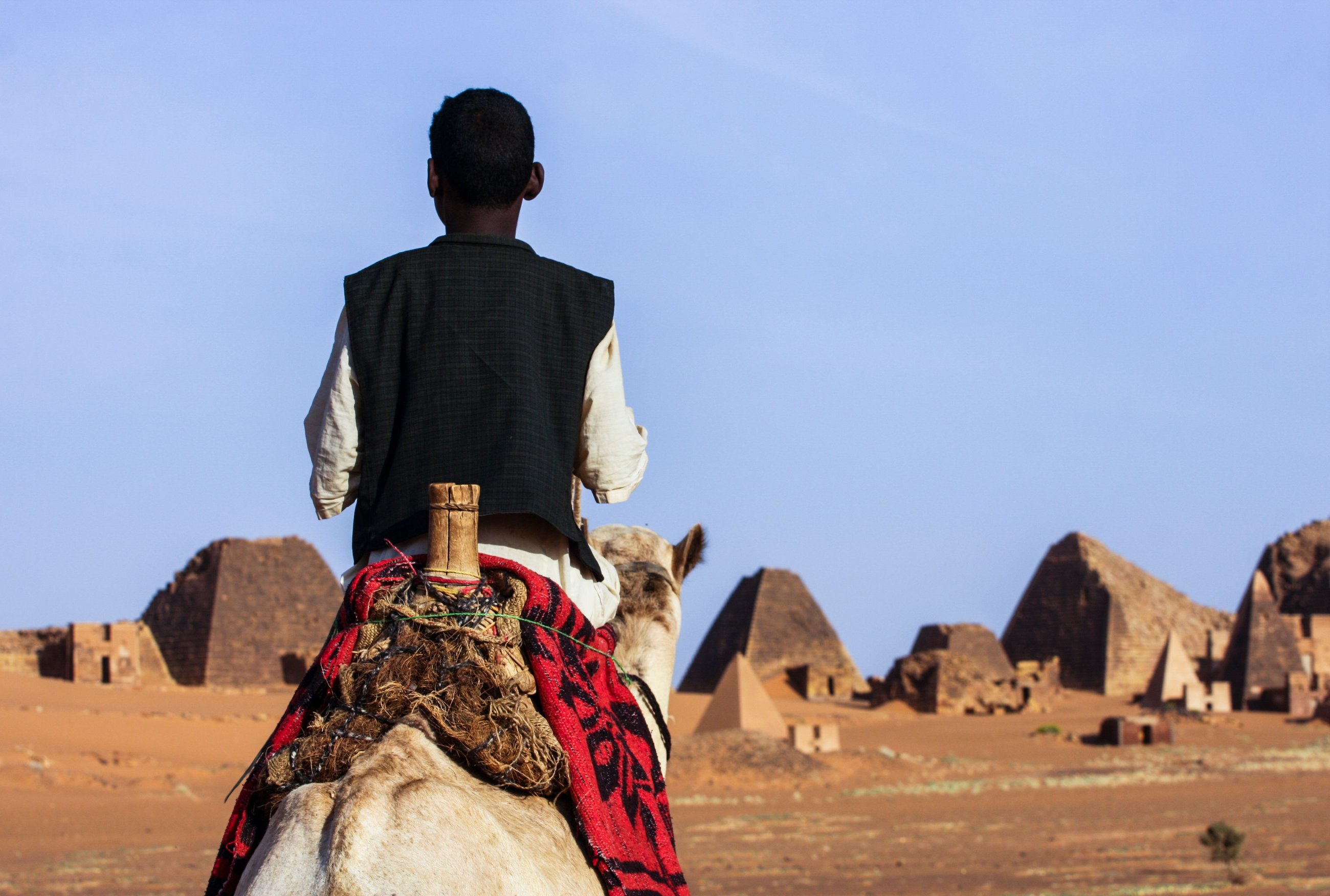 A person riding a camel toward the pyramids of Meroe