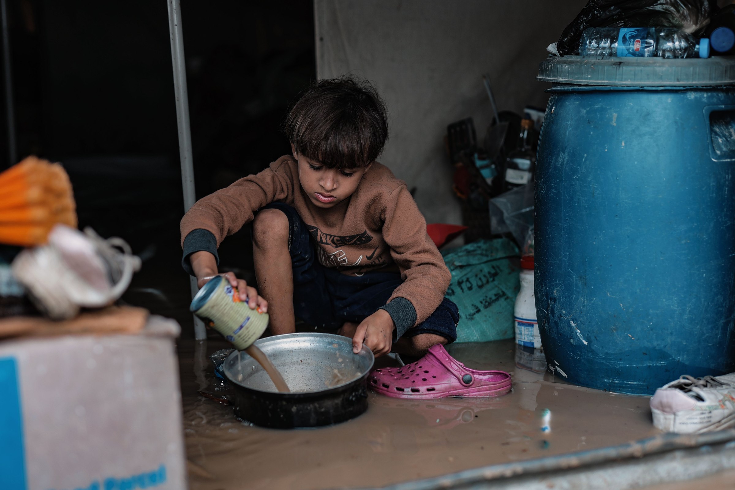 A young boy pours canned food into a pot