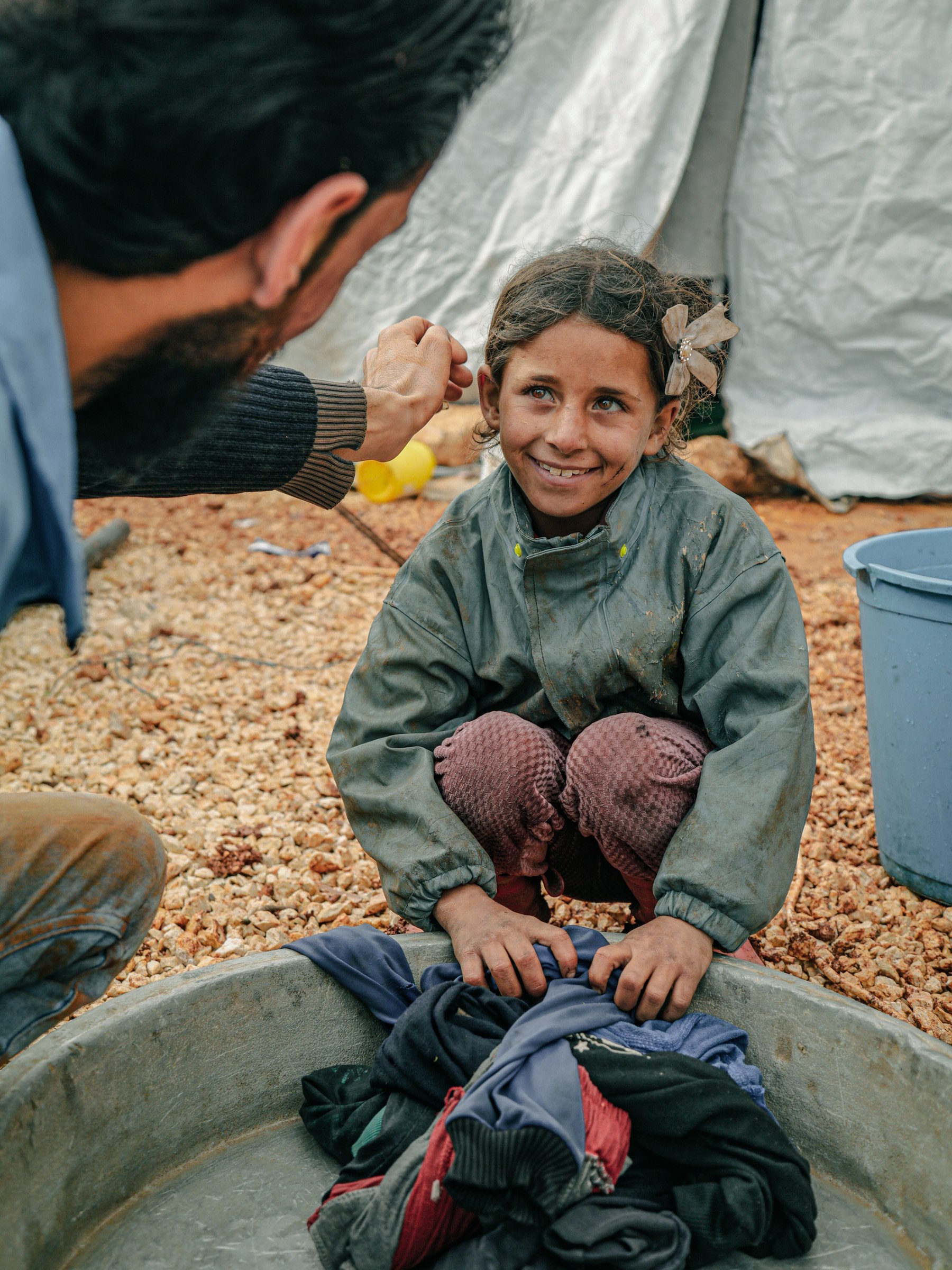 A young girl with a flower hair clip smiles beside a washbasin
