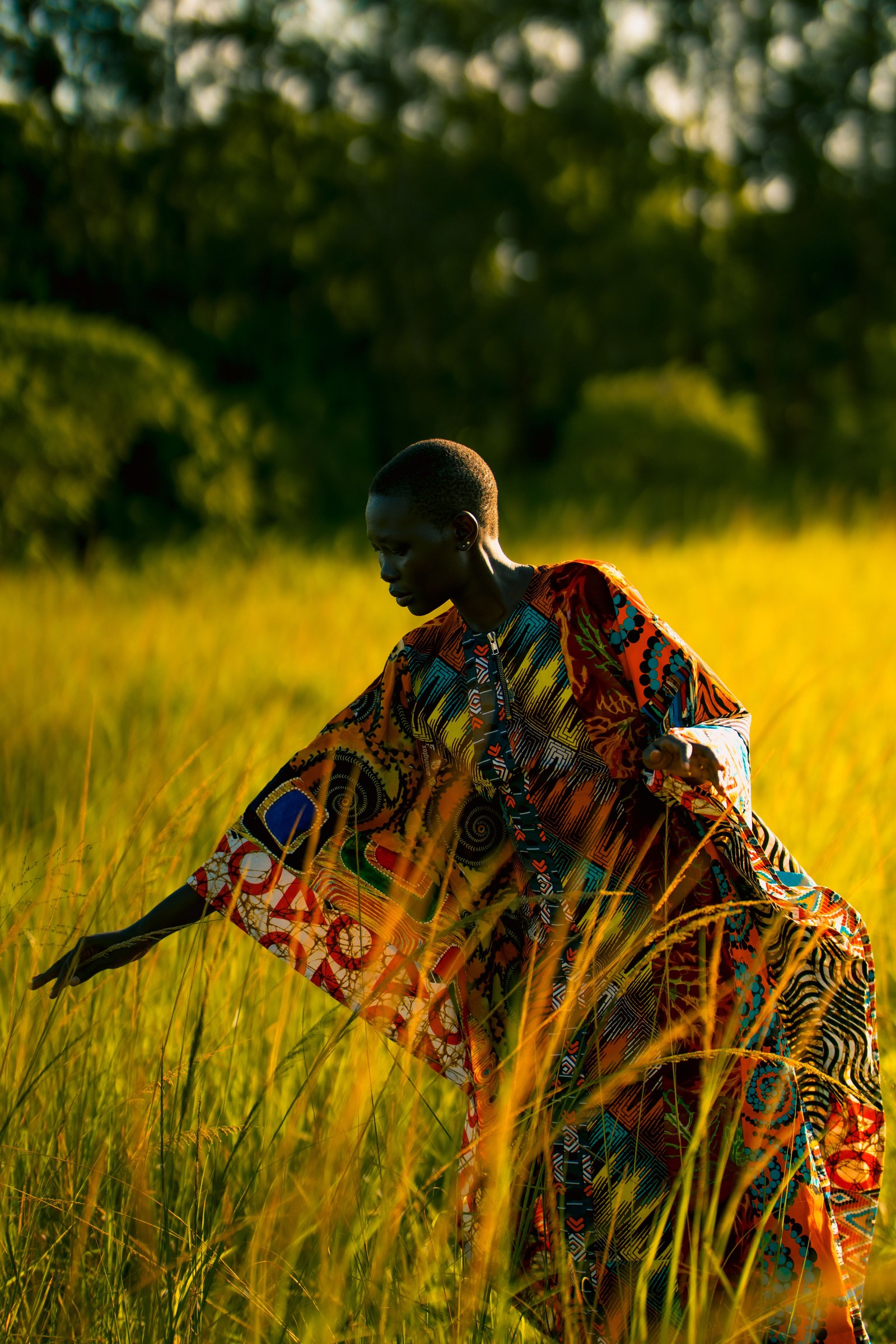 A woman in vivid traditional patterned dress stands in a golden grass field