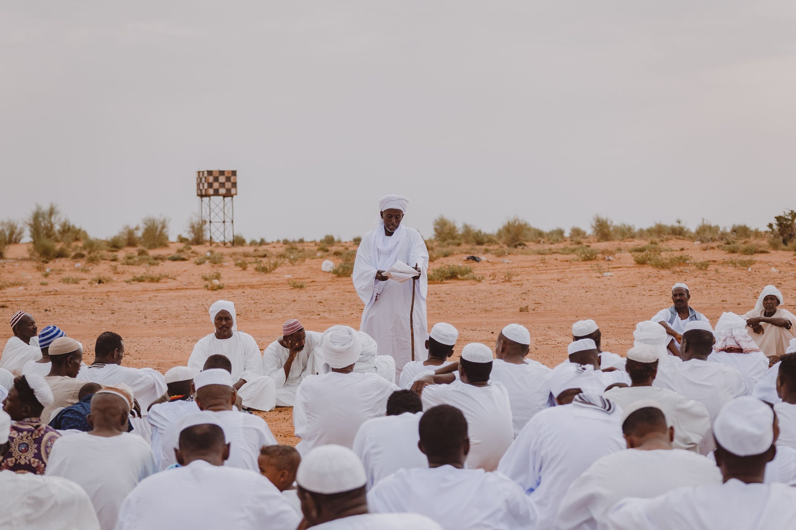 A community elder speaks to a large seated gathering in the desert