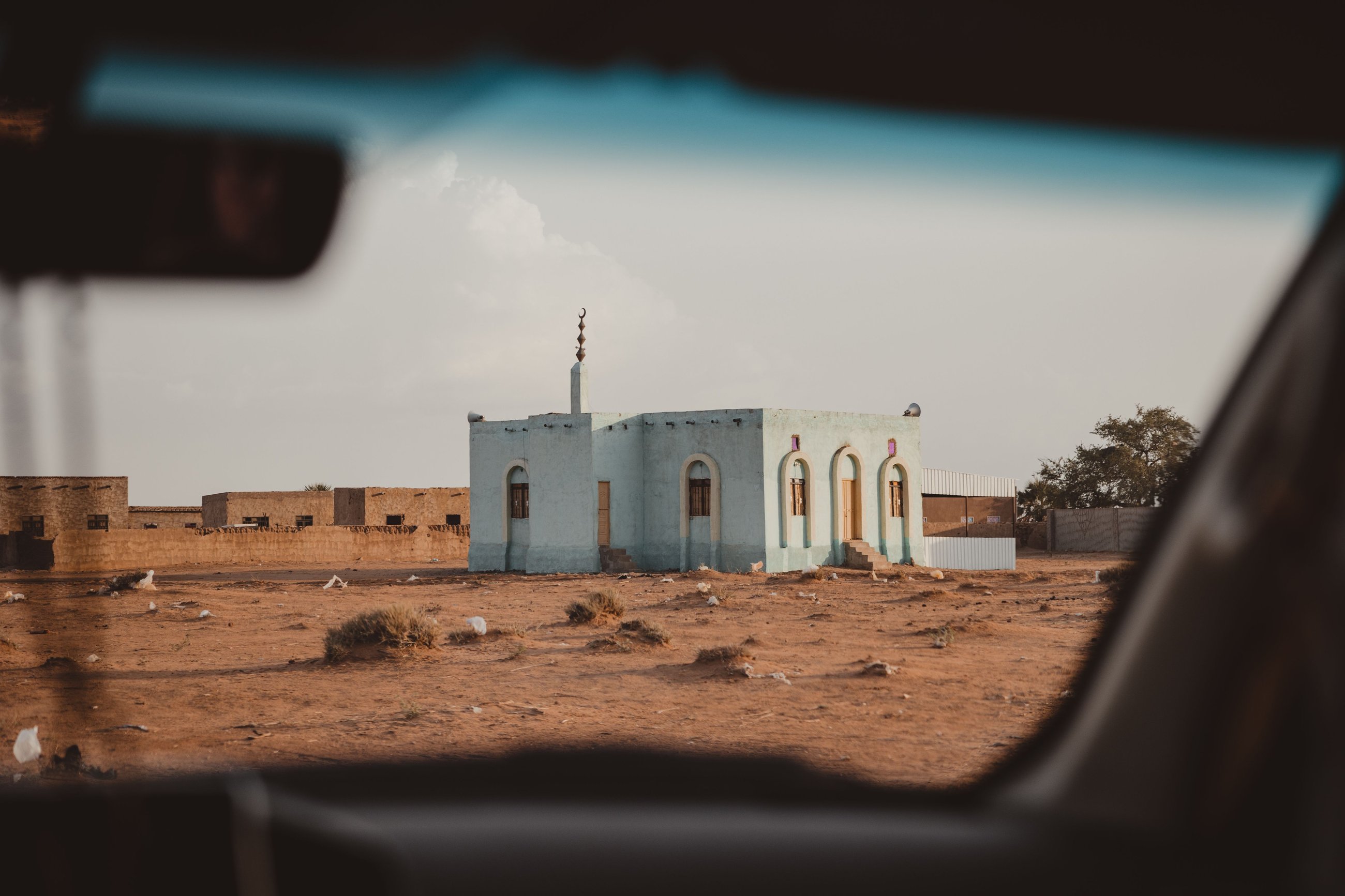 A small blue mosque and village buildings seen from a car window